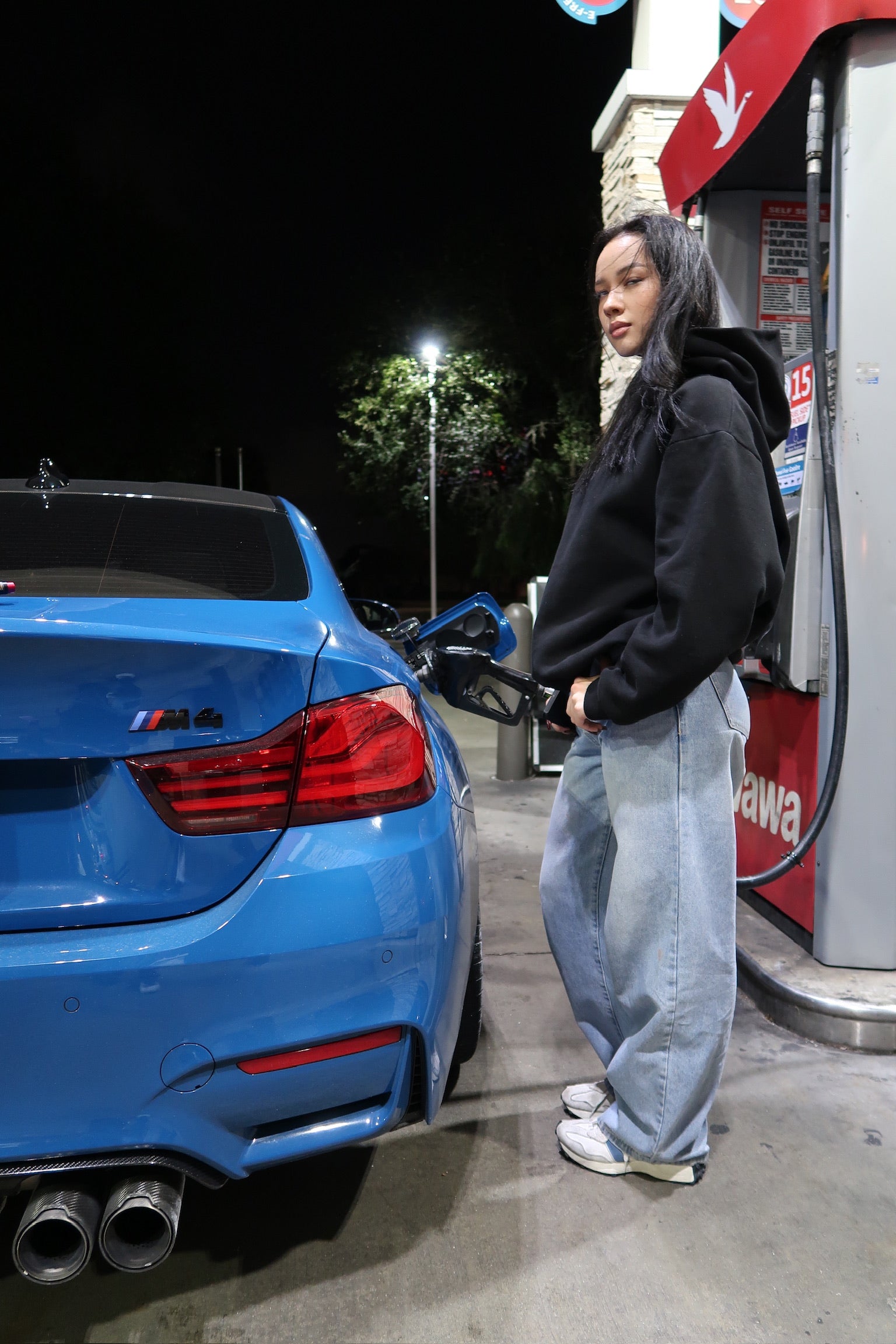 Lifestyle photo featuring the Genzerz Co. hoodie in action, late-night refuel with a blue BMW M4. Designed for motion, built for presence.
