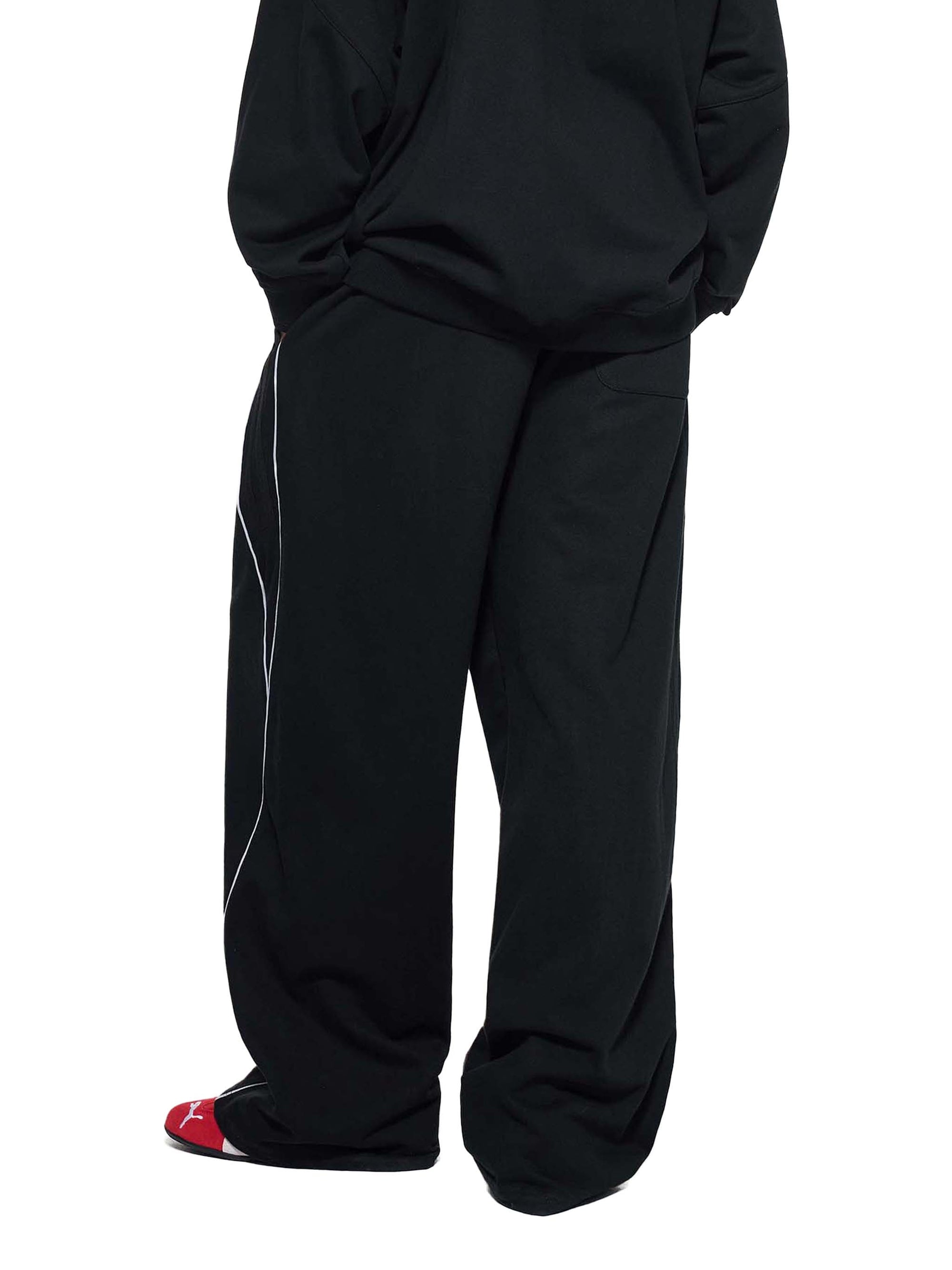 Model wearing black Genzerz wide-leg pants with white stripe detailing and relaxed fit.