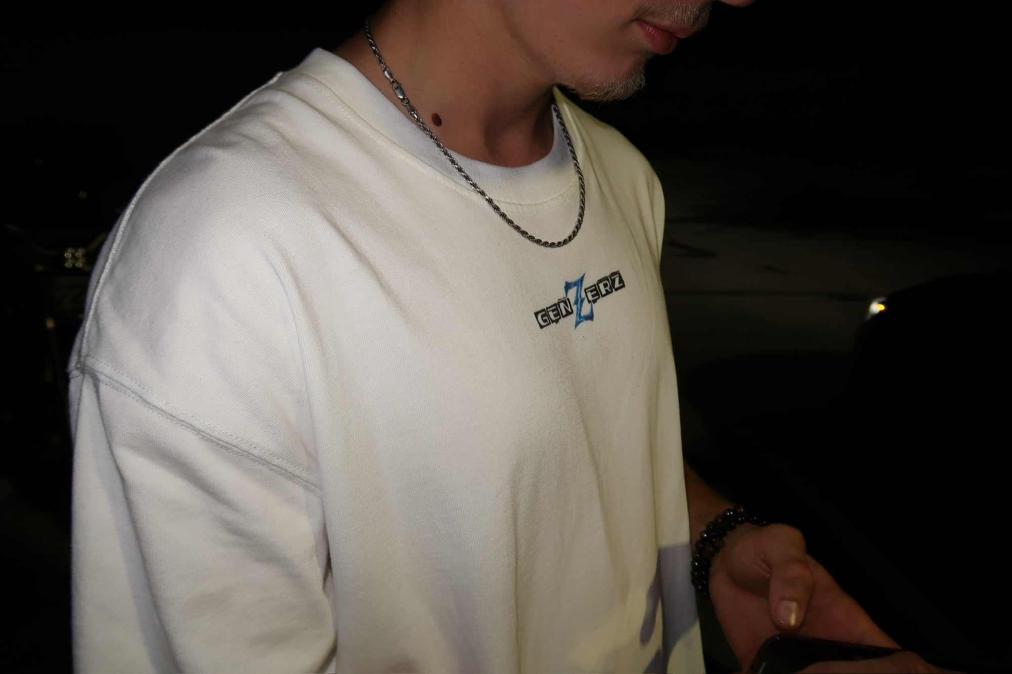 Close-up of a person wearing the Genzerz white Z Tee at night, showing the embroidered logo and minimal streetwear design that defines the brand’s clean, motion-driven aesthetic.