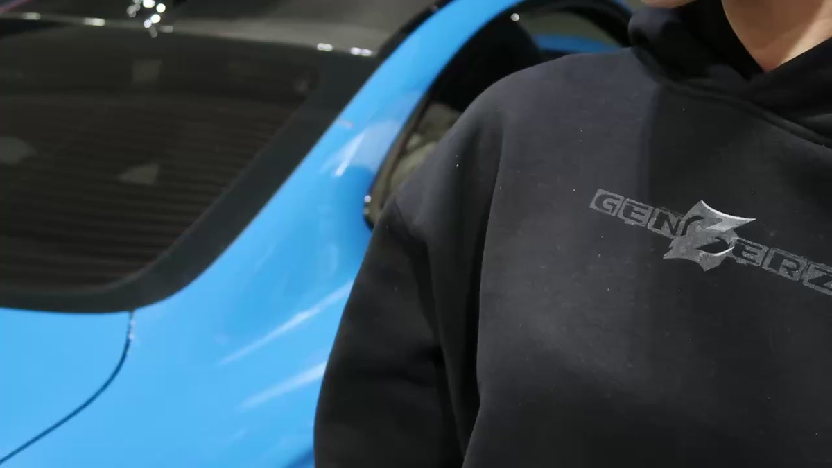 Girl wearing the black Genzerz Racer Z hoodie filling up a blue BMW M4 at a gas station. Close-up shots highlight the oversized Z design on the back, representing Genzerz streetwear lifestyle and motion culture.
